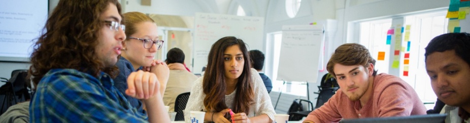 Students around a table looking at a laptop. 