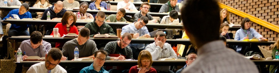 Students in a large classroom with a teacher in the foreground. 