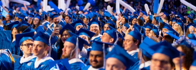 Large group of graduates sitting down with balloons in background. 