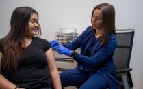 A Student Health Services nurse about to vaccinate a smiling female student. 