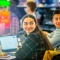 Two students sitting at a table with laptops, looking behind them. 