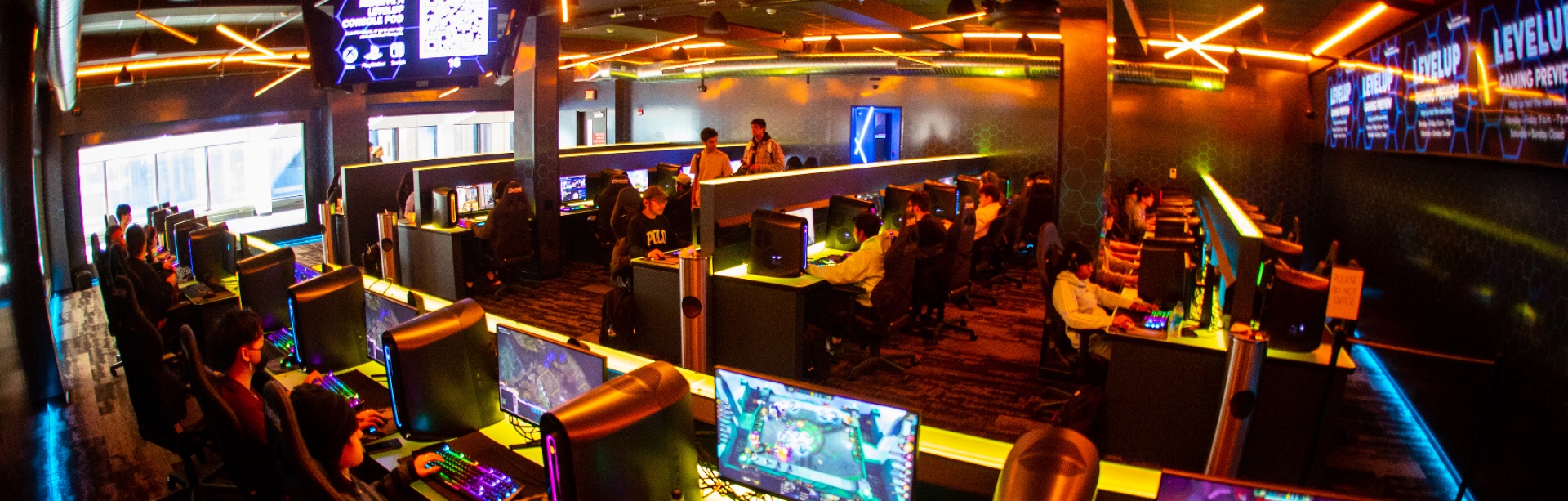 Banks of gaming machines host student gamers in a colorfully-lit space. 